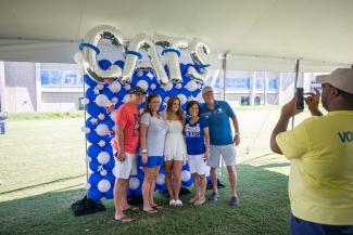Family posing for a photo in front of blue and white balloons that spell out CATS