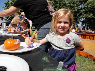 Child painting a pumpkin and smiling