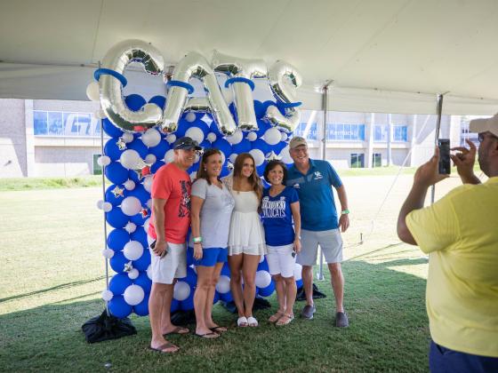 Family posing for a photo in front of blue and white balloons that spell out CATS